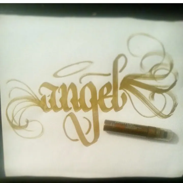 Angel in gold script with long flourishes and a halo, beside a gold marker