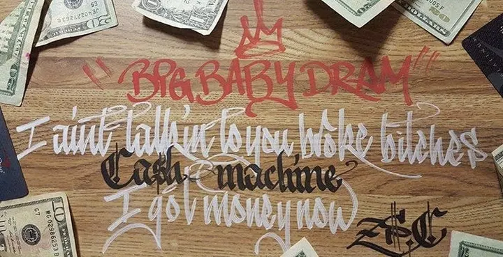 Song lyrics lettered in red, white and black on a wooden table scattered with dollar bills