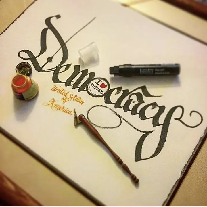 Democracy in black blackletter over United States of America, with an ink pot, a dip pen and a marker