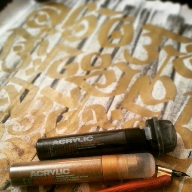 Close-up of gold blackletter on white with acrylic paint markers