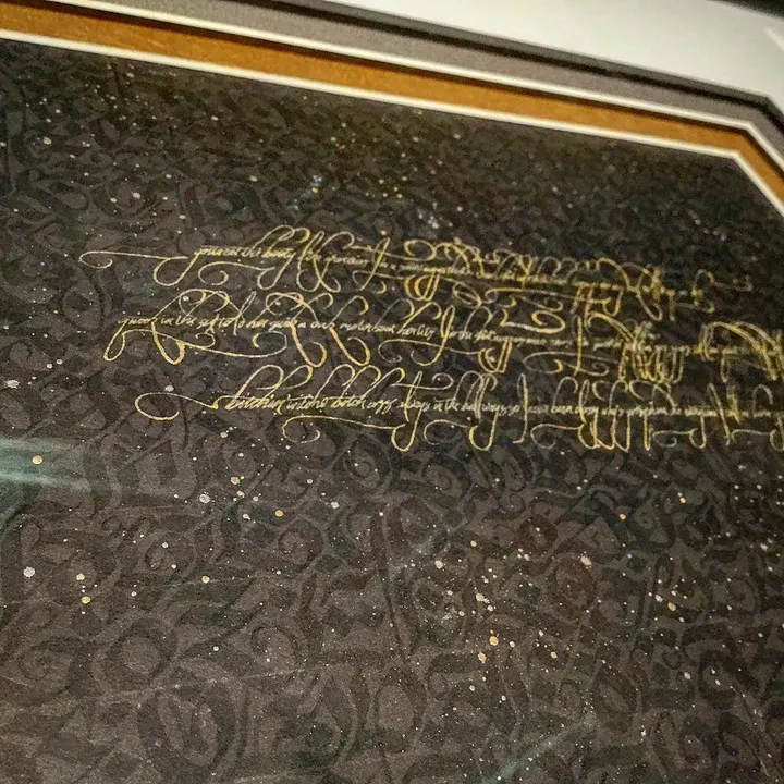Gold calligraphy lines running over black lettering, in a frame