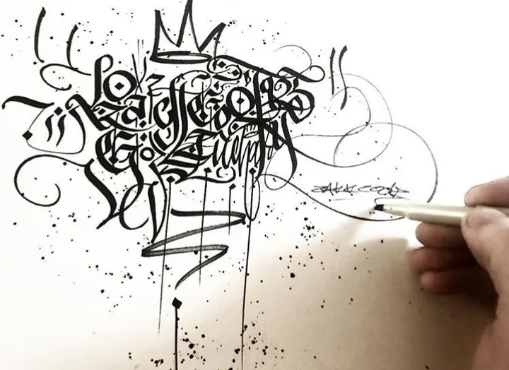 A hand inking a tall stack of blackletter with a calligraphy pen, ink spatter below