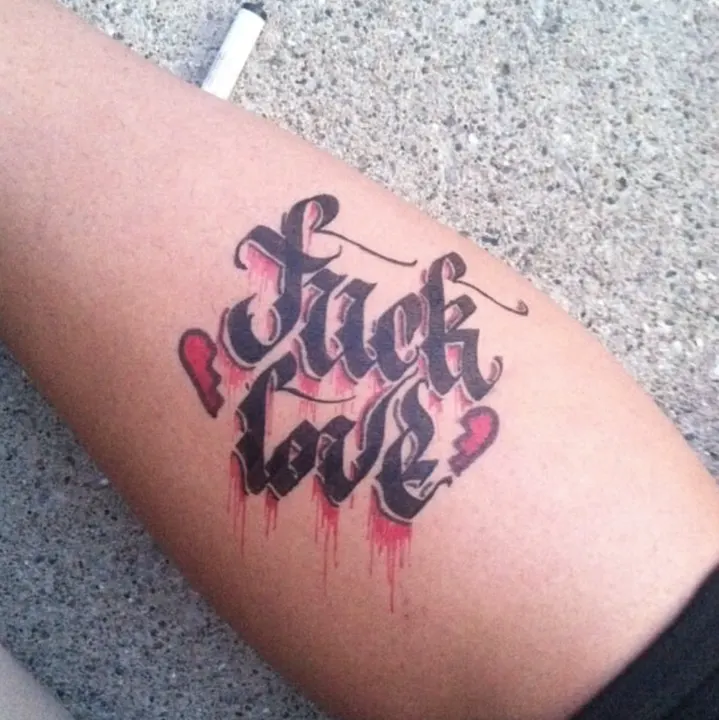Two words lettered in black and red on a forearm, with drips