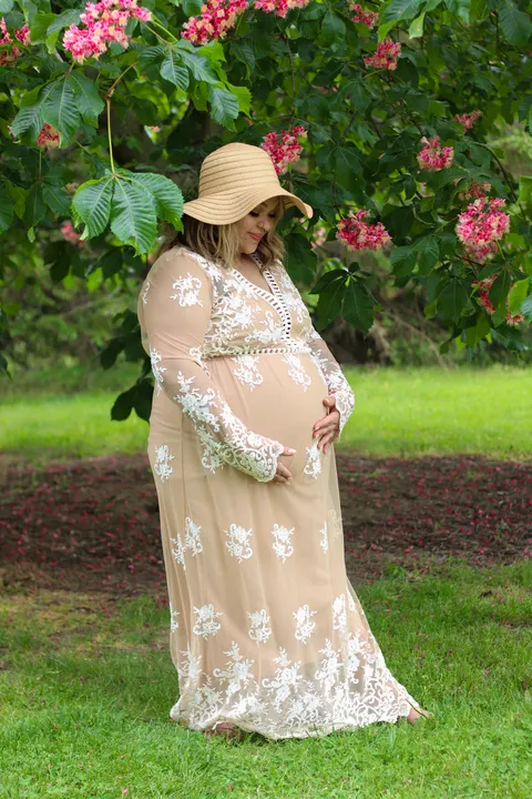 A pregnant woman in a lace gown under a flowering tree