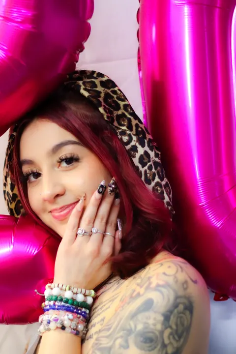 A woman in a leopard hood smiling between pink balloons
