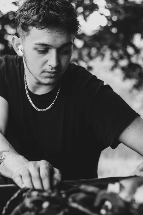 A young man working under a car hood, in black and white