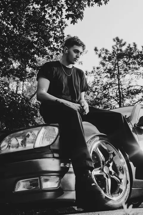 A young man sitting on a Lexus fender, in black and white