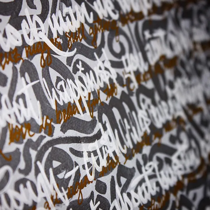 Close-up of white blackletter strokes with gold script running through